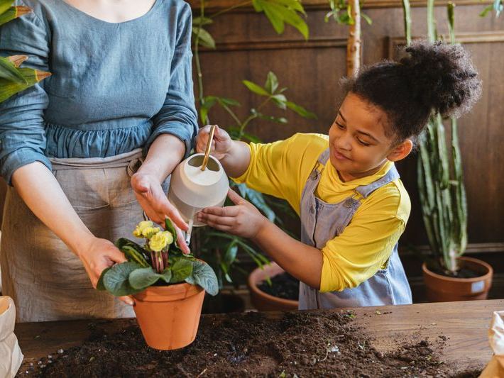 Child and adult watering plants together in a green garden