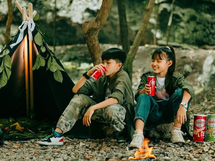 Children camping by a tent with a glowing campfire in the forest