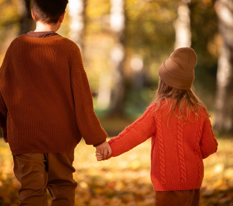 Two children holding hands on an autumn forest path